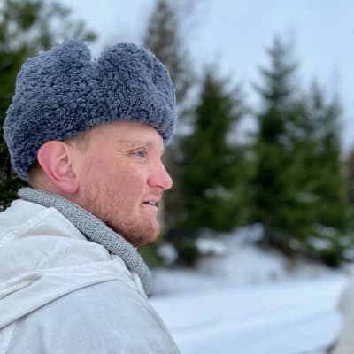 Närbild på mansansikte, fotat från sidan. Han är klädd i finska armens vintermössa från krigstiden, snödräkt och stickad tröja.