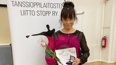 Katja Köngäs står och håller i en blomma, ett diplom och en liten ask.