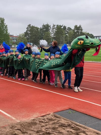 Dickursby skolas barn tågar in på idrottsplanen inne i en jättelik drake.