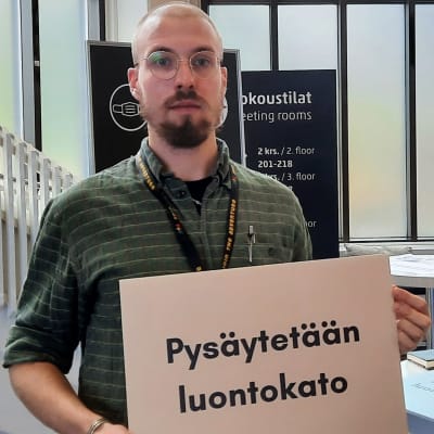 En man håller i en skylt där det står "Pysäytetään luontokato" (översättning: "Låt oss stoppa förlusten av biologisk mångfald")