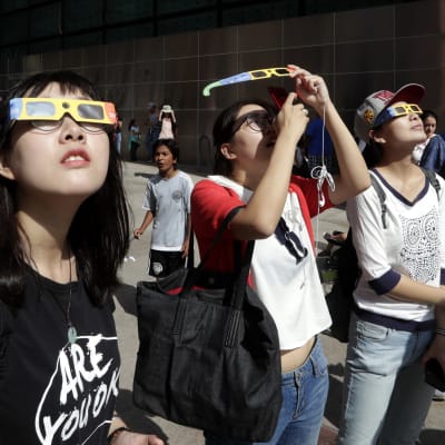 Kiinalaiopiskelijoita katsomassa taivaalle suojalasit silmillään.