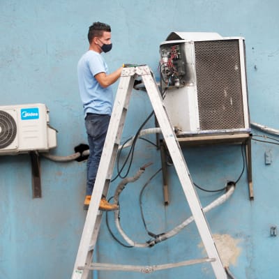 Mies korjaa ilmastointilaitetta Kuubassa.