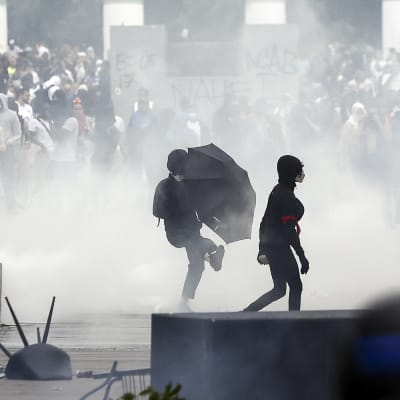 Luften är grå av tårgas när polisen försöker få demonstranter i Paris att skingra sig. På en skylt skymtar man namnet Nahel.