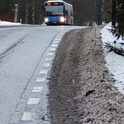 En plogad väg, där cykelfilen är helt täckt av snöslask. I bakgrunden en buss.
