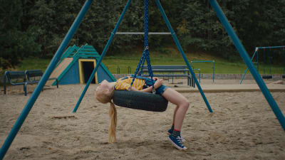En flicka ligger på rygg i en gunga på en lekplats.