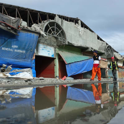 Huomioliiveihin pukeutuneet pelastajat kävelevät maanjärjistyksen runteleman kauppahallin ohi Padadan kaupungissa Filippiineillä. Osa rakennuksen julkisivusta on sortunut järistyksen takia.