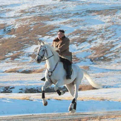 Kim Jong-un rider på en häst som rusar fram över ett snöbeklätt landskap. 