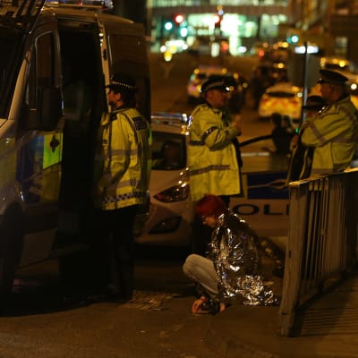 Kvinna sitter på trottoarkanten efter händelsen i Manchester och polisen finns på plats.