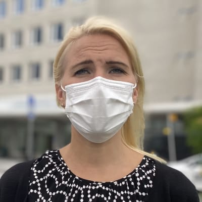 Medelålderskvinna med axellångt blont hår och munskydd tittar in i kameran.