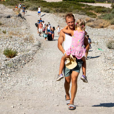 Turister evakueras längs med en grusväg. En man bär en flicka i sin famn.