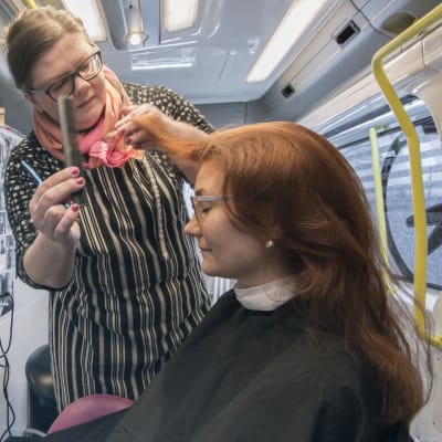 Nainen kampaa asiakkaan hiuksia parturiautossa