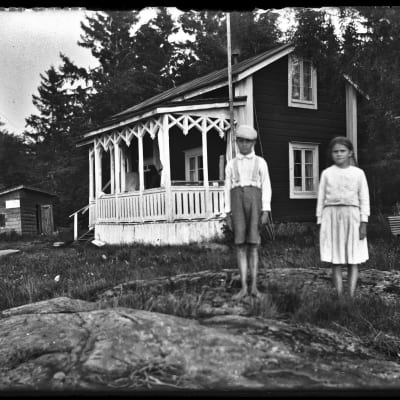 Svart-vit bild av två barn framför ett sommarhus.