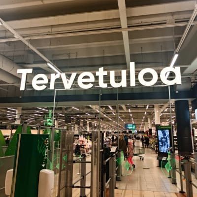 Prisman sisäänkäynnin portit. Ylhäällä suuri tervetuloa-teksti, oikealla infopiste.