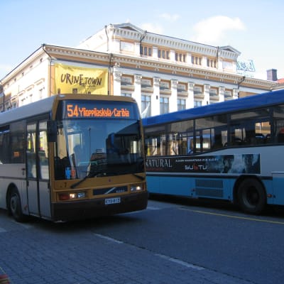 Två stadsbussar vid Salutorget i Åbo. I bakgrunden finns Åbo Svenska Teater.