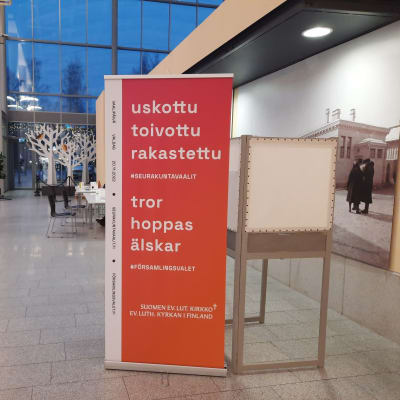 En röd skylt vid ett valbås vid församlingsvalet. På skylten står "uskottu, toivottu, rakastettu, tror, hoppas, älskar".
