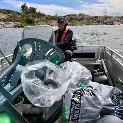 En äldre man, Folke Österman kör sin båt. I båten finns stora mängder plastavfall. Bland annat plastpåsar och trasiga trädgårdsstolar.