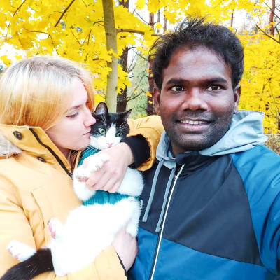 En kvinna med en katt i famnen poserar tillsammans med en leende man. Bakom dem syns gula höstlöv.