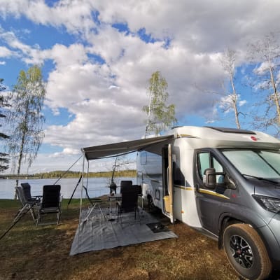 En husbil parkerad på en grön gräsmatta framför en blå insjö