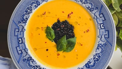 En blåvit tallrik med orange morotssoppa toppad med svarta belugalinser.
