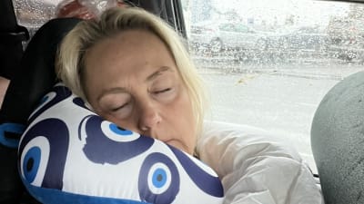 En kvinna sover på en kudde i en bil. Det regnar utanför.