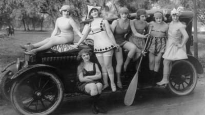 En grupp kvinnor poserar vid en bil. Svartvit bild.