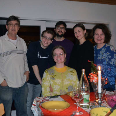 Familj på fem personer står och sitter vid ett bord.
