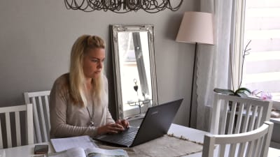 Ela Strandberg sitter vid sitt vita matbord hemma vid sin dator.