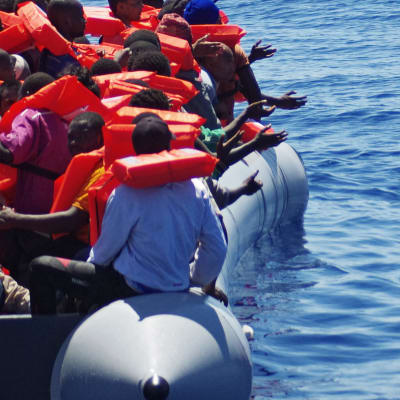 Räddningsarbetare kastar vattenflaskor till flyktingar på en gummibåt på Medelhavet.