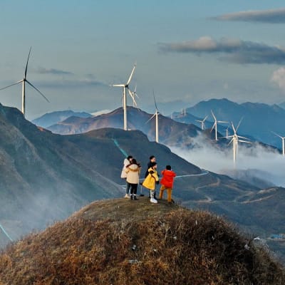 En grupp människor står på en topp i en bergskedja som bekläs av vindturbiner. 