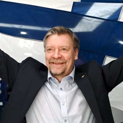 Jukka Jalonen poseeraa Suomen lipun kanssa.