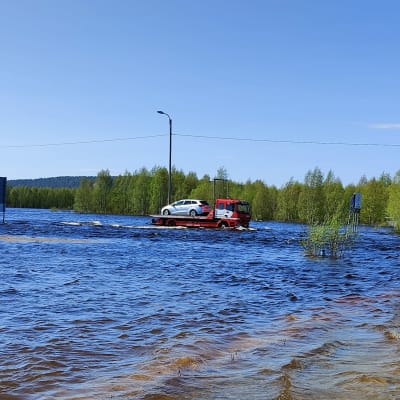 Hinausauto kuljettaa lavallaan henkilöautoa tulvaveden keskellä