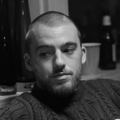 En man och en kvinna sitter på en soffa, kvinnan i förgrunden ur fokus och med ansiktet bortvänt. Mannen tittar på henne med en öm blick.