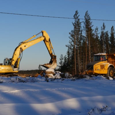 Kaksi työmaakonetta – kaivuri ja jumpperi – talvimaisemassa KymiRingin moottoriratatyömaalla.