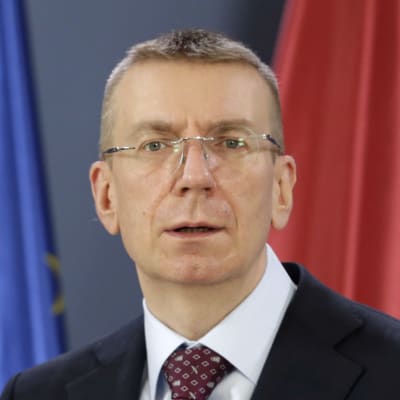 Lettlands utrikesminister Edgars Rinkēvičs framför en mikrofon. I bakgrunden EU:s och Lettlands flaggor.