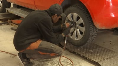 En person byter däck på en röd bil i en verkstad. 