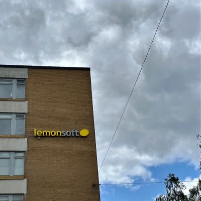 Kerrostalo Vaasan keskustassa, jossa toiseksi ylimmän ikkunan vieressä Lemonsoft-valomainos. Tummia pilviä taustalla.