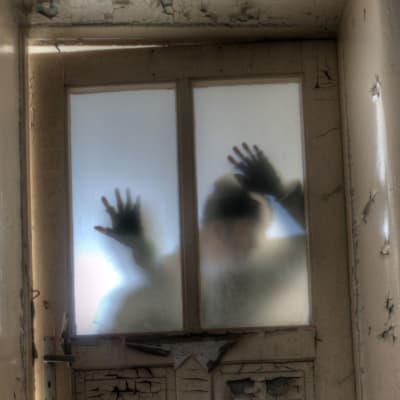 En man med händerna på glaset syns bakom en sned och dimmig dörr.