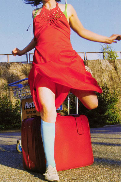 Kvinna i röd klänning och med röd resväska på marken intill.