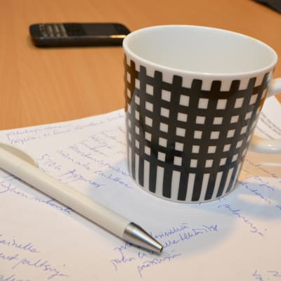 Kynä, kahvimuki ja muistiinpanoja paperilla