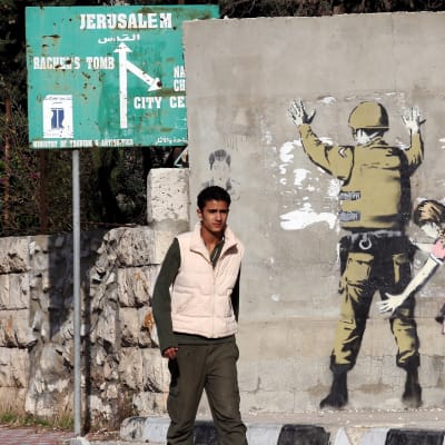 Mies kävelee ohi seinän, johon on maalattu sotilas ja häntä tarkastava tyttö.