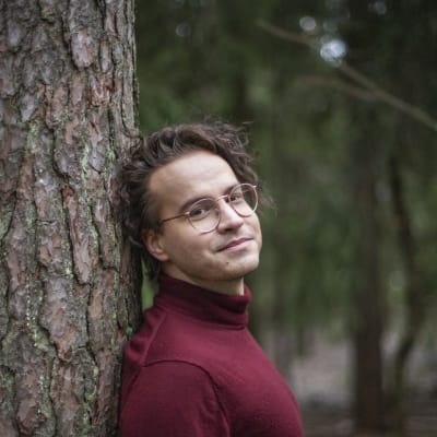 Janne Hirvasvuopio står utomhus, lutad mot en trädstam. 