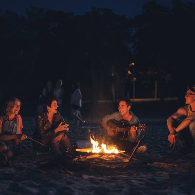 Fyra glada männsikor sitter och musicerar runt en lägereld i sommarnatten.