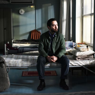 Khaled (Sherwan Haji) sitter på en säng i en flyktingscentral och ser ut genom fönstret.