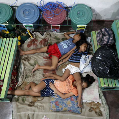 Kolme lasta nukkuu koulun lattialla patjoilla evakossa hirmumyrskyn takia Filippiineillä.