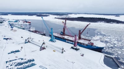 Vingar till ett vindkraftsverk lyfts av ett fartyg i en hamn.