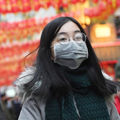 Två kvinnor går på en gata i London dekorerad med kinesiska dekorationer. Båda bär munskydd.