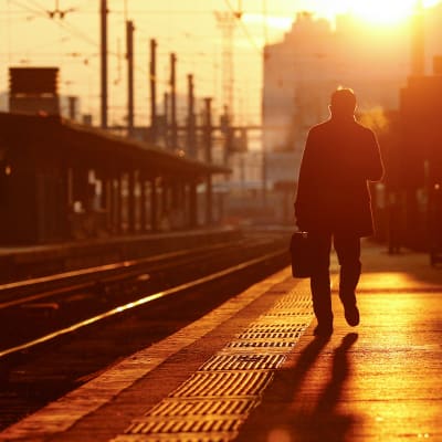 Yksinäinen mies auringonnousun aikaan tyhjällä junalaiturilla.