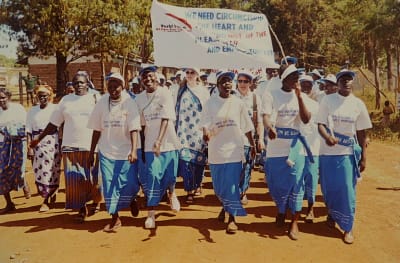 En grupp kvinnor som går med ett plakat genom en by i Afrika