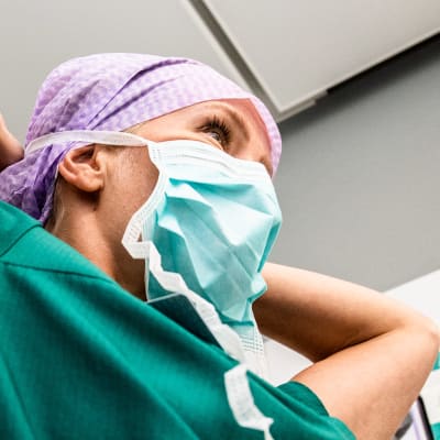 en kvinna i grönblå sjukvårdsdräkt och munskydd i en sjukhusmiljö
