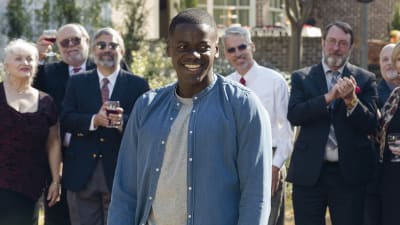 Chris (Daniel Kaluuya) står leende omringad av vita mänskor.